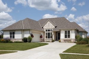 White suburban house with beige stone details, double garage, concrete driveway, and front lawn under partly cloudy sky.