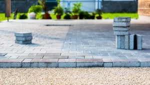 Close-up of partially installed concrete pavers over gravel base with stacked bricks and a taut leveling string line.