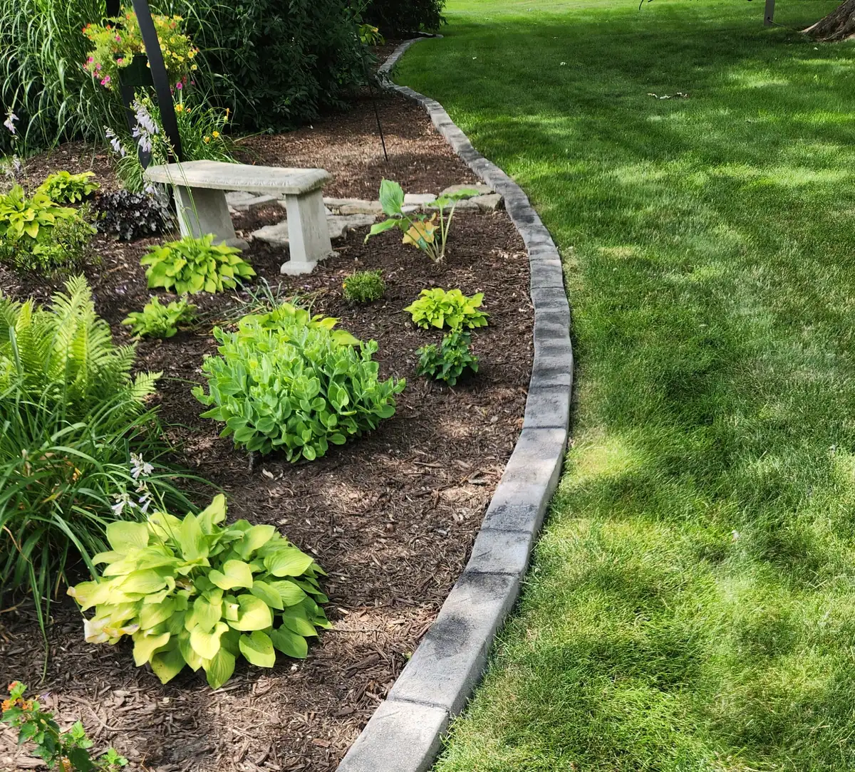Decorative rock landscaping borders a brick home, featuring light gravel, small shrubs, and a stamped concrete edge.