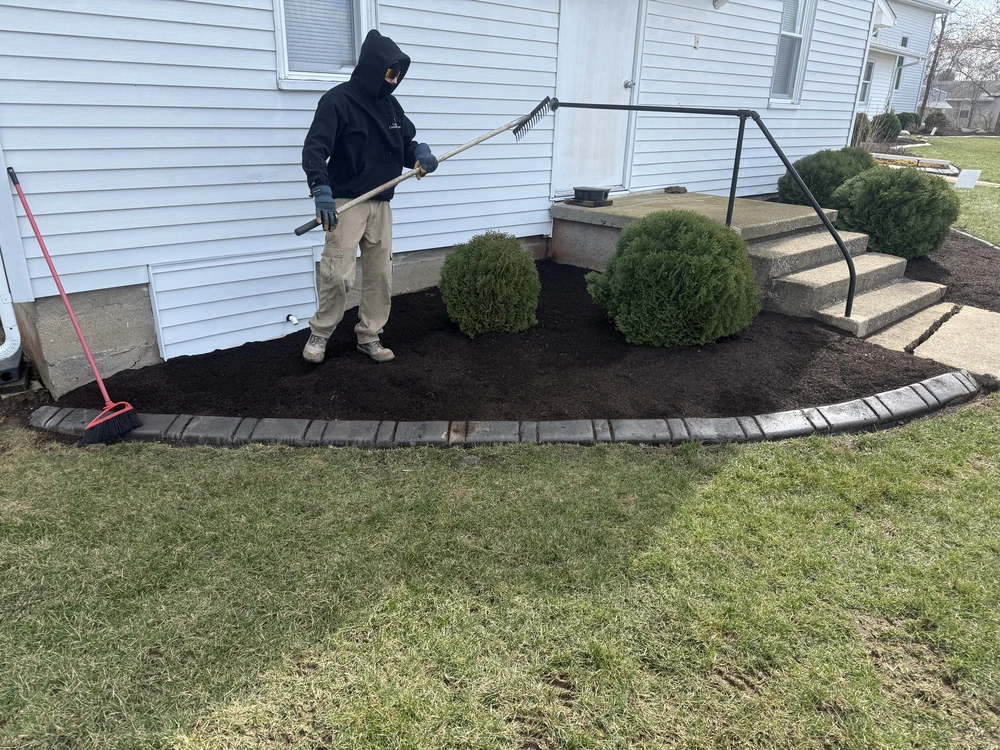 Worker performing winter lawn maintenance by refreshing mulch beds to protect roots and reduce mud damage after thaw.
