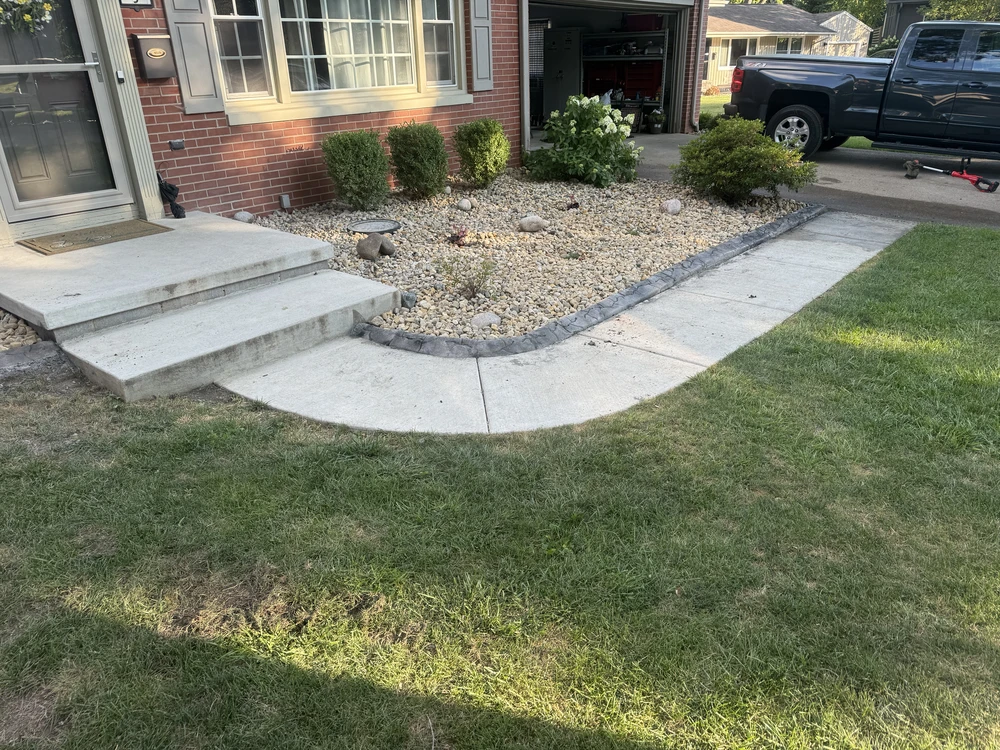 Curved front patios and walkway by landscaping bed, checking concrete edges for winter cracks and heaving.