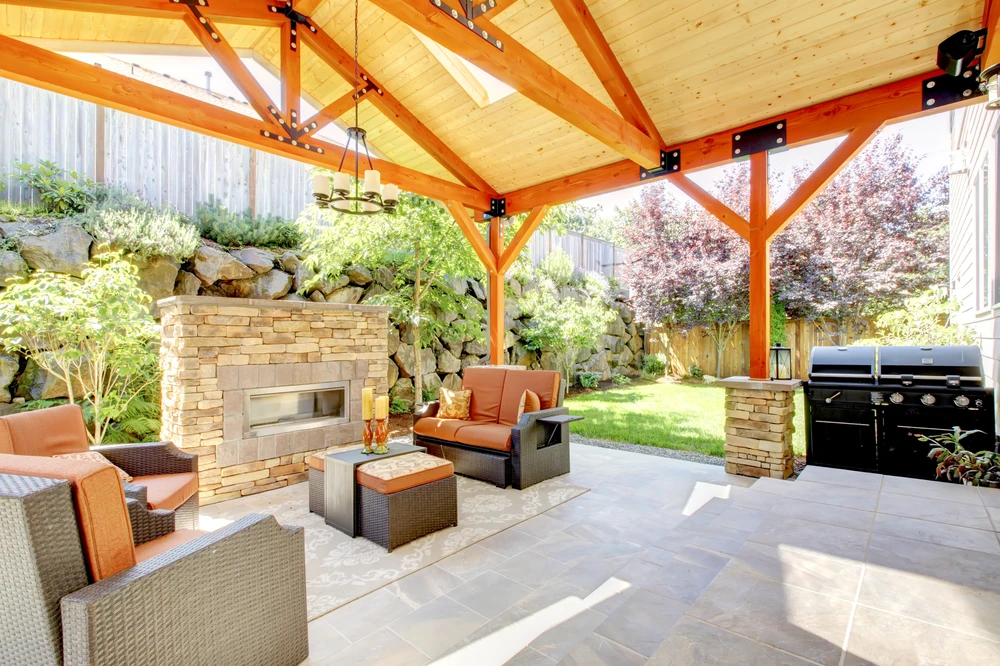 Covered patio with stone fireplace, seating, grill, and wood beams creating a polished hardscaping retreat.