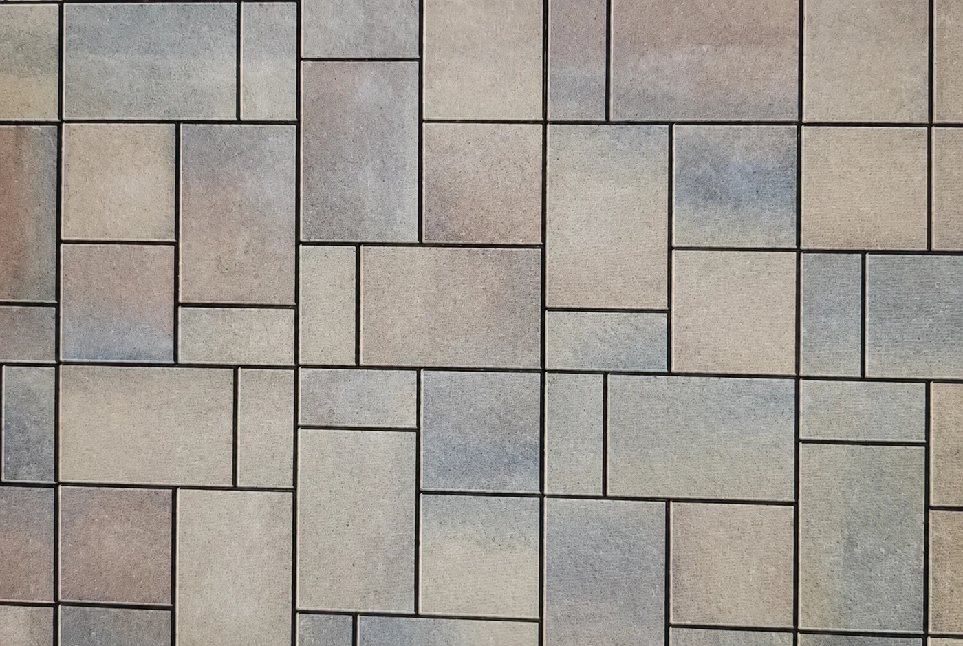 Close view of mixed-size rectangular pavers in tan, gray, and muted brown tones arranged in a modular pattern.