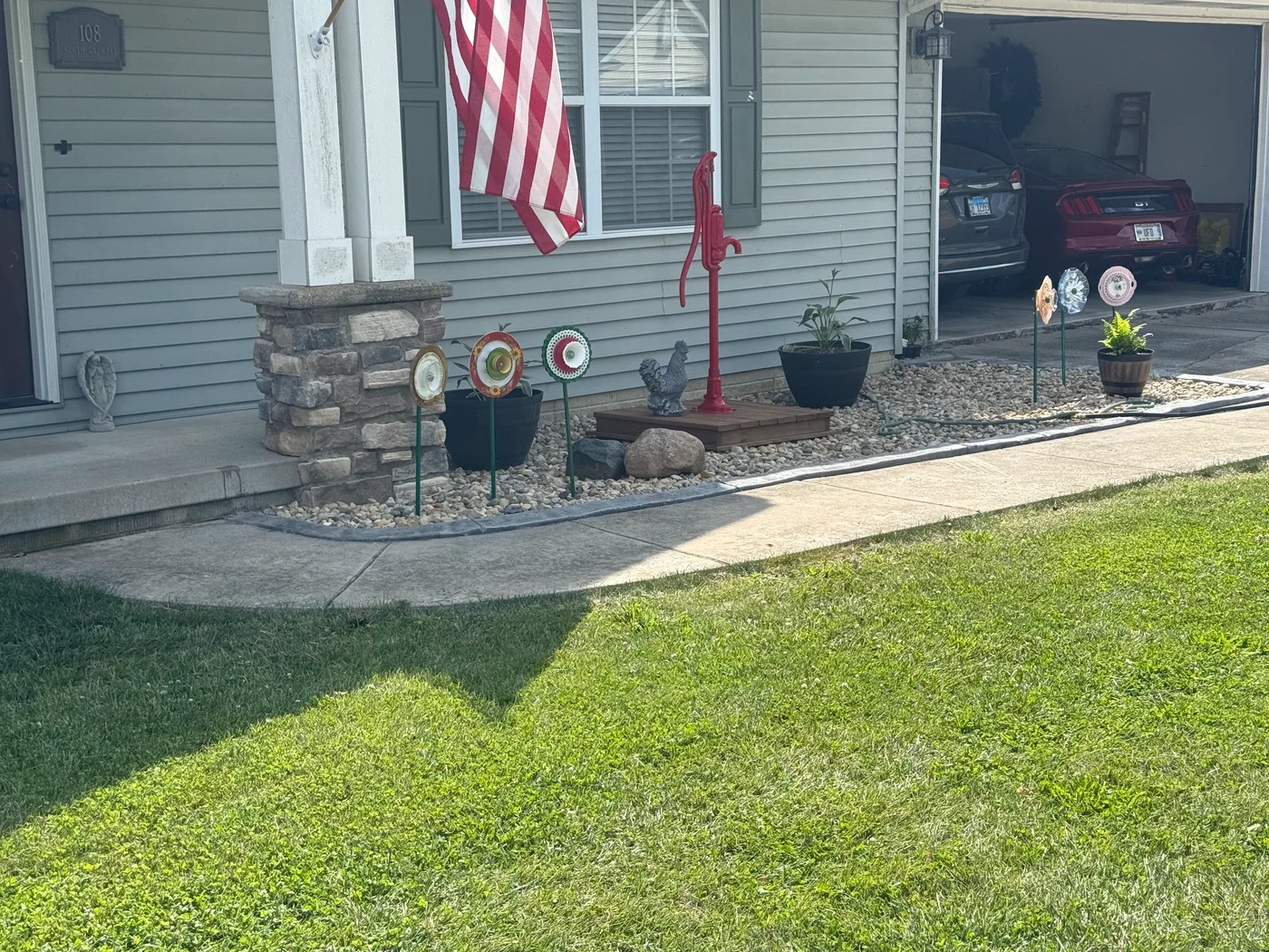 Green front lawn beside a gray-sided home with a curved concrete walkway and light rock landscaping.