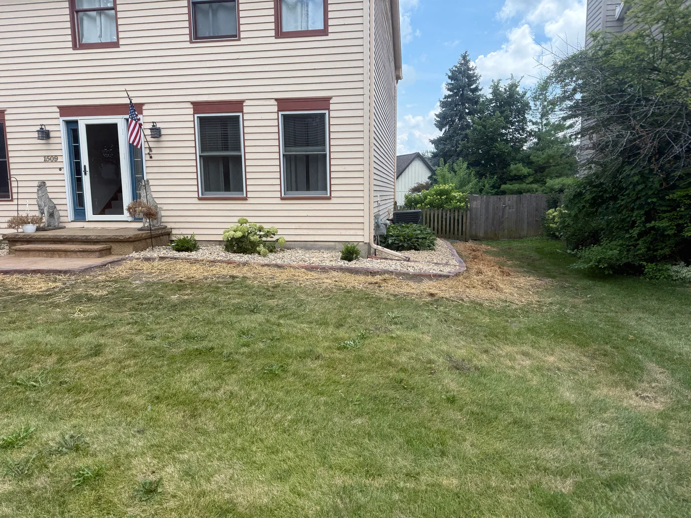 Tan-sided home with a light rock landscape bed, small shrubs, hydrangea, and green lawn.